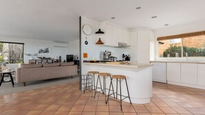 Una cocina moderna con armarios blancos, una isla central con taburetes y un amplio ventanal con vistas al exterior.
