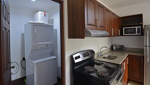 Kompakti keittiö, jossa on puukehikoiset kaapit, sisäänrakennettu mikroaaltouuni, liesi ja pesukone.