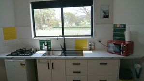 A kitchen with a gas stove, sink, and a microwave. There is a window with a view of trees and a road.