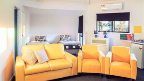 A modern room with a curved yellow sofa, a small table, and a kitchenette area.