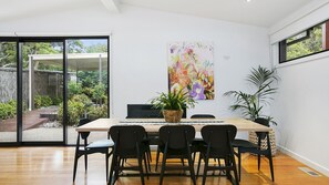 A modern dining area with a wooden table, black chairs, and a large abstract painting on the wall. - Pet Friendly - Miss Maude Mt Martha with pool and spa (Mount Martha)