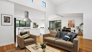 A spacious living area with a high ceiling, a kitchen with white cabinets, and a dining area with a table and chairs. - Pet Friendly - Miss Maude Mt Martha with pool and spa (Mount Martha)