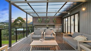 A covered outdoor seating area with a wooden deck, metal-framed chairs, a sofa, and a table. - Pet Friendly - Miss Maude Mt Martha with pool and spa (Mount Martha)