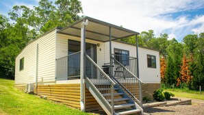 A single-story mobile home with a covered porch, a staircase, and a small patio area.
