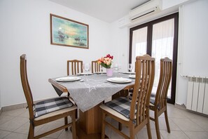 Uma sala de jantar com mesa posta para quatro pessoas, cadeiras com assentos acolchoados, um quadro na parede e uma janela com cortinas.