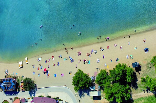 Une vue aérienne d’une plage avec des personnes, des parasols et des bateaux.