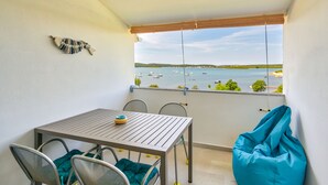 Een balkon met een tafel en stoelen, een blauwe loungestoel en uitzicht op boten op het water.