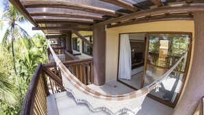 A wooden balcony with a hammock, large sliding glass doors, and a view of palm trees. - Flat high standard in the seaside paradise in Barra de São Miguel (Barra de São Miguel)