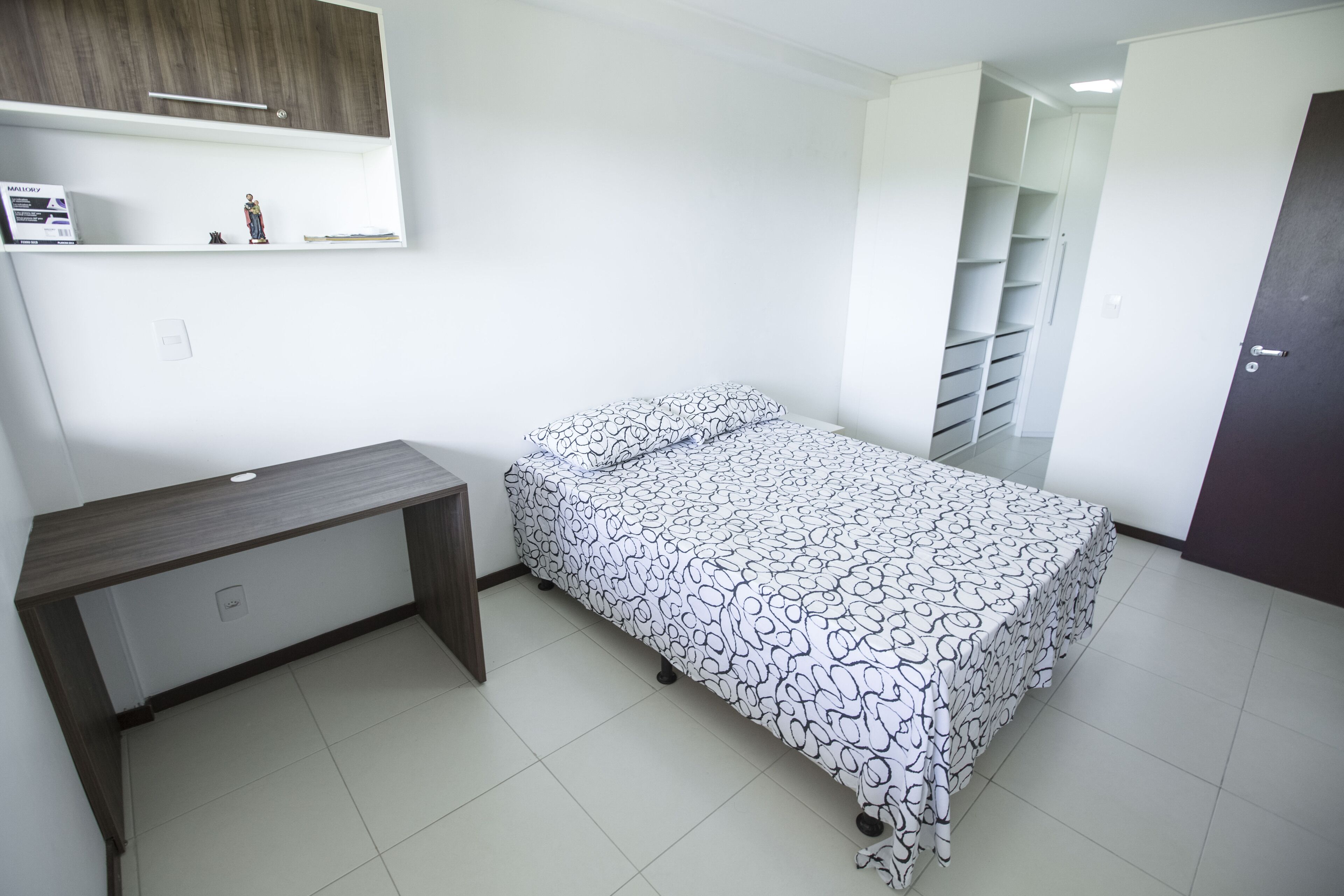 Une chambre à coucher comprenant un lit, un bureau, une armoire et une petite étagère ornée d’objets décoratifs.