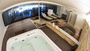 A spa area with a hot tub, seating area, and a glass wall offering a view of the lobby. - Flat high standard in the seaside paradise in Barra de São Miguel (Barra de São Miguel)