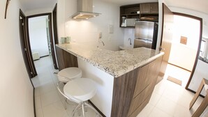 A modern kitchen with a granite countertop, stainless steel appliances, and two bar stools. - Flat high standard in the seaside paradise in Barra de São Miguel (Barra de São Miguel)
