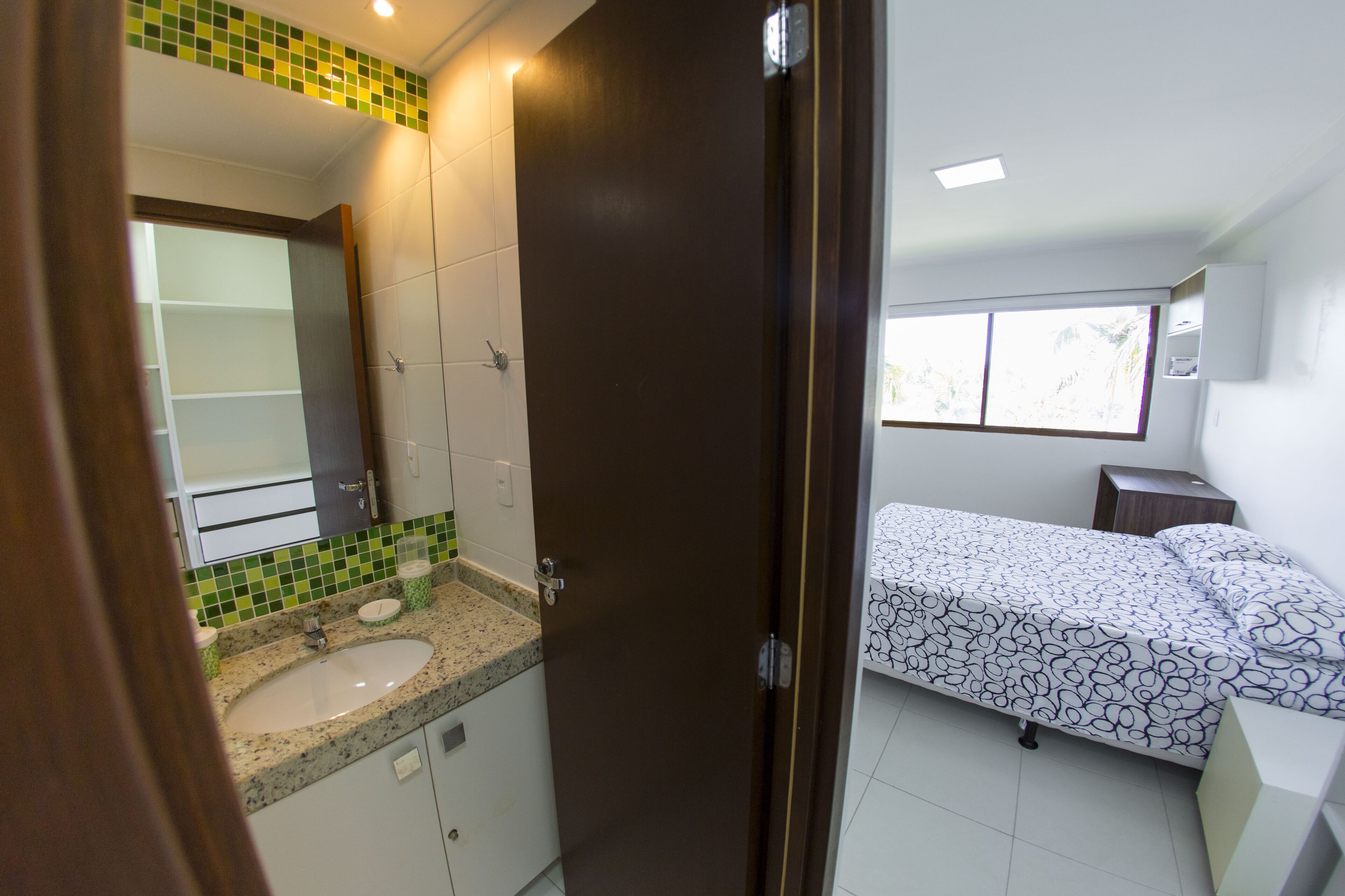 Un dormitorio con cama, ventana y baño con lavabo y espejo.
