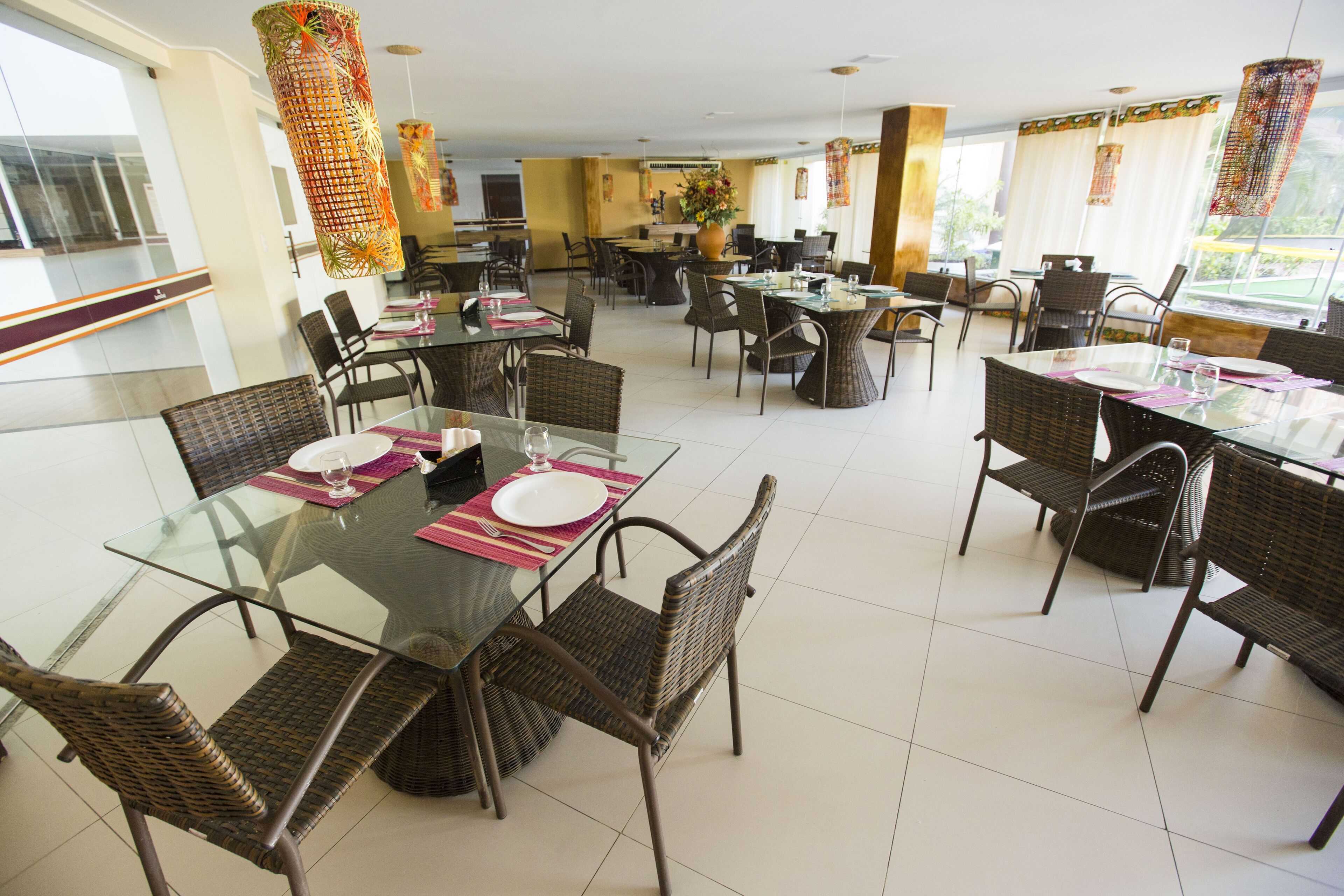Un comedor espacioso con varias mesas y sillas, ventanas amplias y un diseño interior moderno.