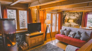 Ein gemütliches Blockhaus-Interieur mit Kamin, Fernseher, Sofa und Steinwand.