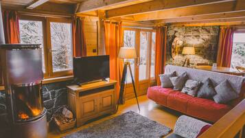 L’intérieur d’un chalet chaleureux, avec une cheminée, un téléviseur, un canapé et un mur en pierre.