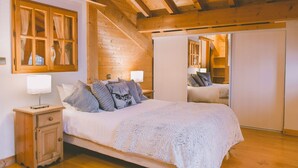 Ein Schlafzimmer mit Holzboden, einem großen Bett mit weißer Decke, einem Nachttisch mit Lampe und einem Kleiderschrank mit Spiegel.