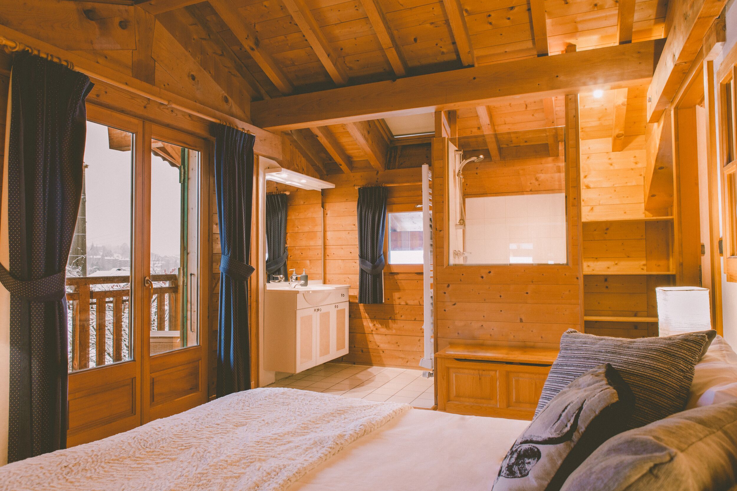 Une chambre dans une cabane en bois, avec un lit, une petite table de chevet et une fenêtre avec des rideaux.
