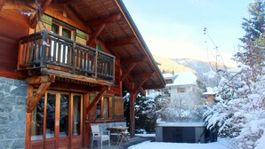Eine Holzhütte mit Balkon, Steinmauern und Whirlpool in verschneiter Landschaft.