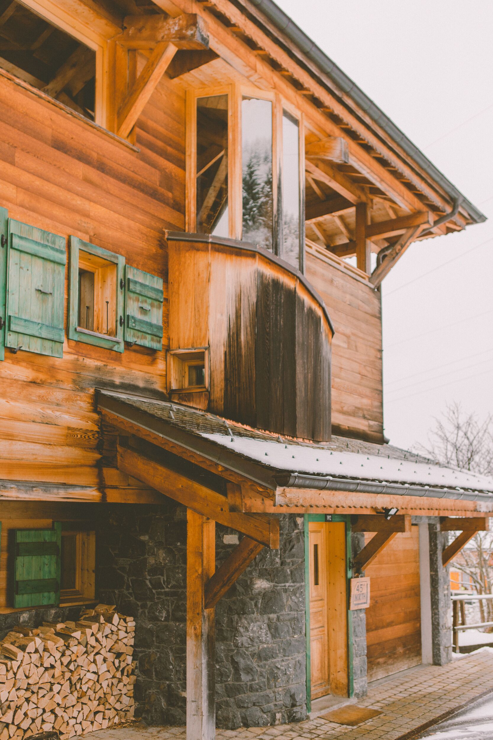 Une construction en bois, avec des fondations en pierre, un balcon en bois et une pile de bois de chauffage à l’extérieur.