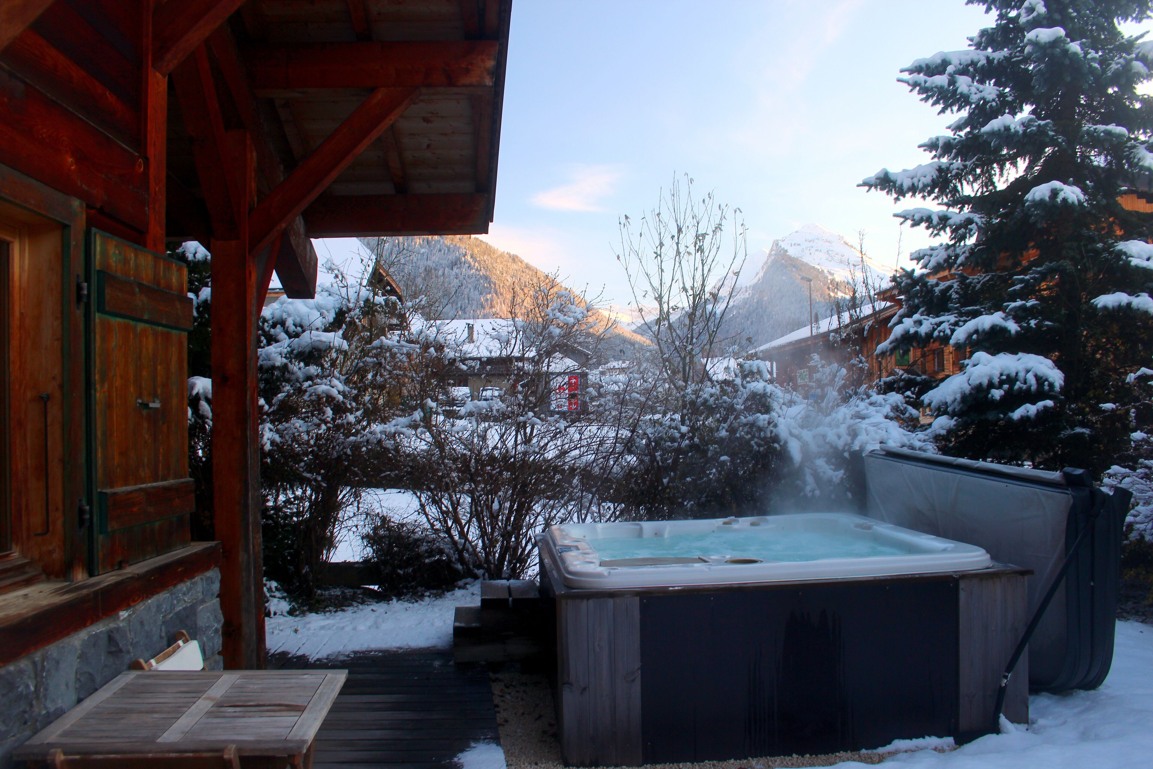 Une cabane en bois avec un bain à remous, située dans un espace extérieur enneigé.