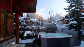 Une cabane en bois avec un bain à remous, située dans un espace extérieur enneigé.