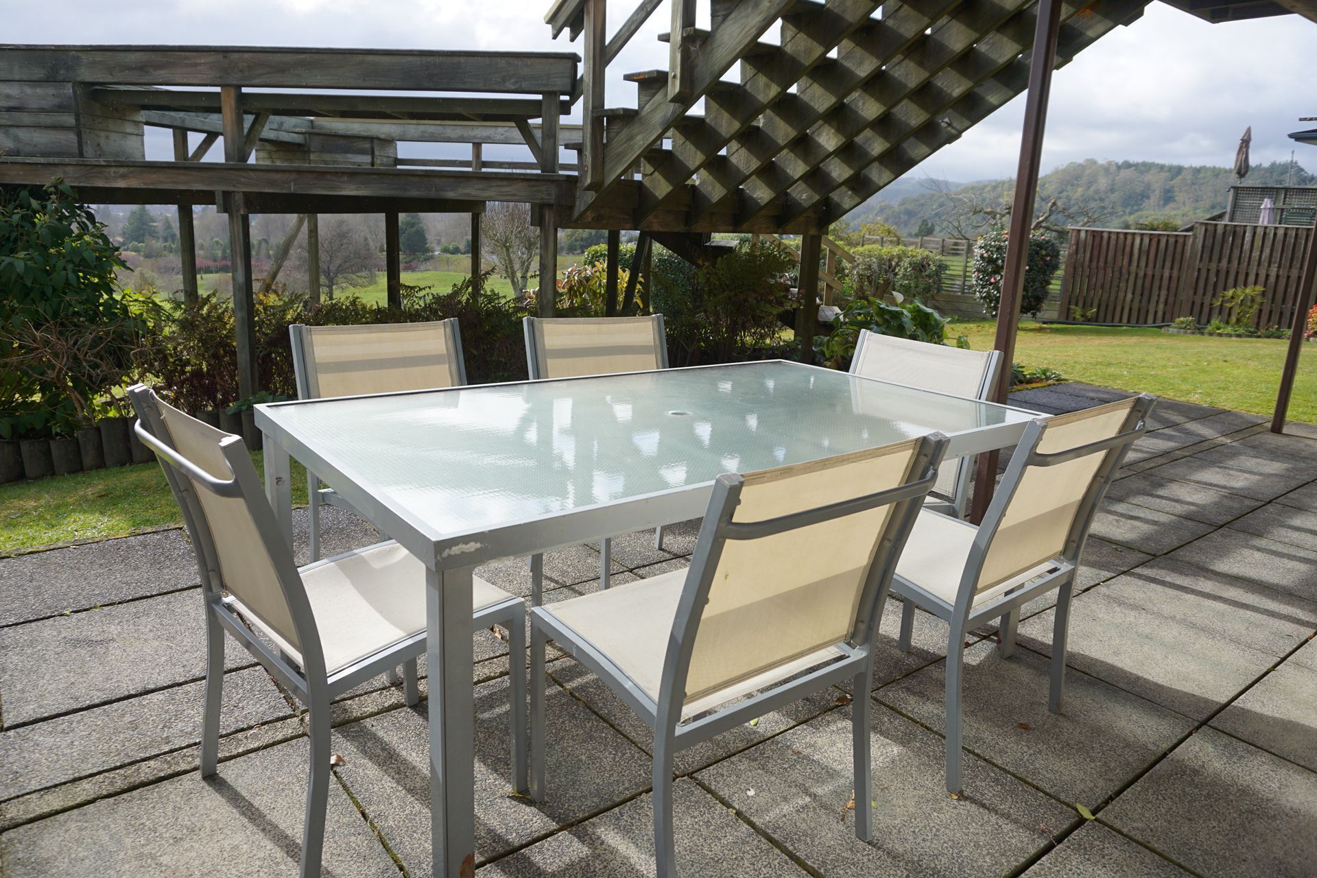 Un patio con una mesa de vidrio y cuatro sillas, rodeado por una pérgola de madera y vistas a un paisaje montañoso.