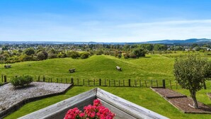 A rural landscape with rolling green hills, a fenced area, and a distant view of a town.