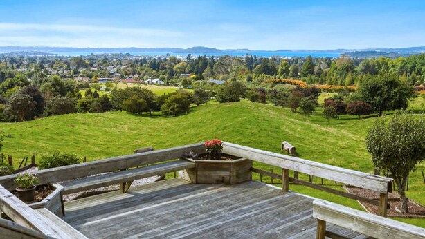 A wooden deck with a bench and planter, overlooking a lush green landscape with trees and a distant town.