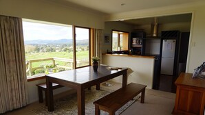 A spacious kitchen with a large window, a dining area with a wooden table and bench, and a view of the countryside.