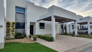Um edifício moderno com telhado plano, área de estacionamento coberta e gramado bem cuidado.