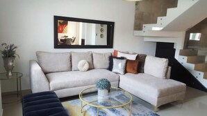Uma sala de estar com um sofá bege, uma mesa de centro redonda e uma escada.