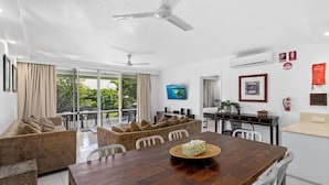 Uma sala de estar moderna com uma mesa de jantar de madeira, sofás bege e uma janela grande com cortinas.