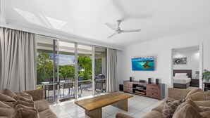 Uma sala de estar moderna com sofá, mesa de centro de madeira, televisão e ventilador de teto.