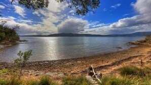 A lakeside view with a rocky shoreline, a wooden walkway, and distant mountains under a partly cloudy sky.
