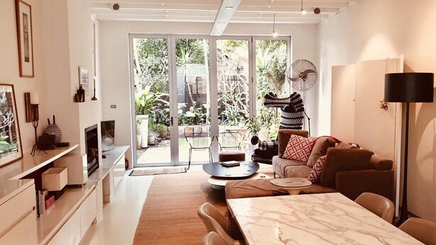 A modern living room with a sofa, coffee table, and dining table. There is a sliding glass door leading to a garden. - The Abode - 2-3 bedrooms - premium, spacious, light-filled and harbour views (Birchgrove)