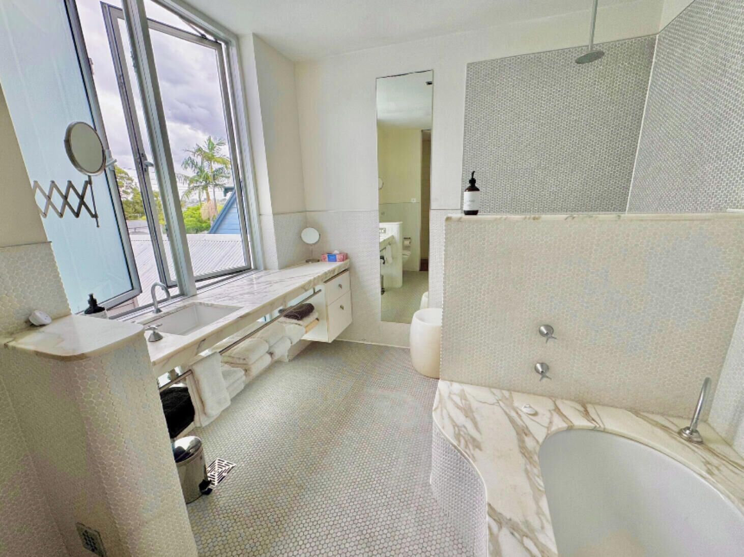 A bathroom with a large window, a sink, a mirror, a toilet, and a shower area.