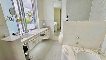 A bathroom with a large window, a sink, a mirror, a toilet, and a shower area.
