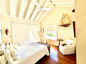 A room with a bed, a chair, a small table, a window with a view, and a ceiling fan.