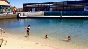 A swimming pool area with a sandy beach, a lifeguard tower, and a building with large windows. - The Abode - 2-3 bedrooms - premium, spacious, light-filled and harbour views (Birchgrove)