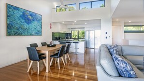 A spacious living area with a dining table, chairs, a sofa, and a large abstract painting on the wall. - Pinnacle 2, Seaview Apartment on Hamilton Island (Hamilton Island)