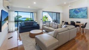 A modern living room with a large sofa, a coffee table, and a dining area with a table and chairs. - Pinnacle 2, Seaview Apartment on Hamilton Island (Hamilton Island)