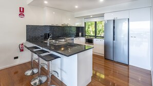 A modern kitchen with a black countertop, stainless steel appliances, and a bar stool. - Pinnacle 2, Seaview Apartment on Hamilton Island (Hamilton Island)