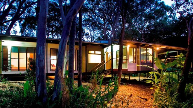 A series of cabins with large windows, surrounded by trees and a wooden deck.
