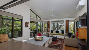 A modern living room with a large window, a ceiling fan, and a flat-screen TV.