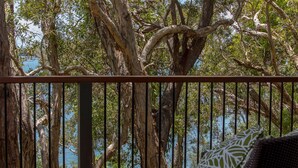 A balcony with a view of the sea, surrounded by trees.