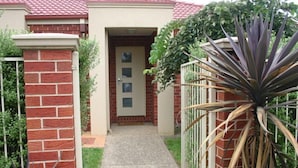 A residential house with a red brick exterior, a beige door, and a concrete pathway leading to the entrance.