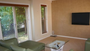 A living room with a green sofa, a glass coffee table, and a flat-screen TV mounted on the wall.