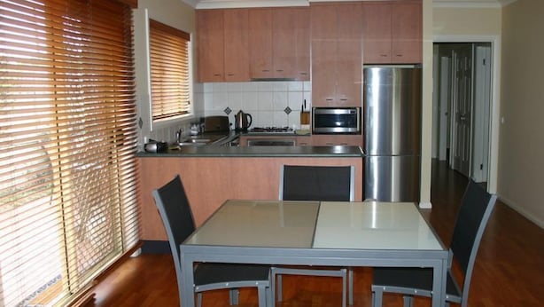A compact kitchen with wooden cabinets, a stainless steel refrigerator, a microwave, and a dining table with chairs.