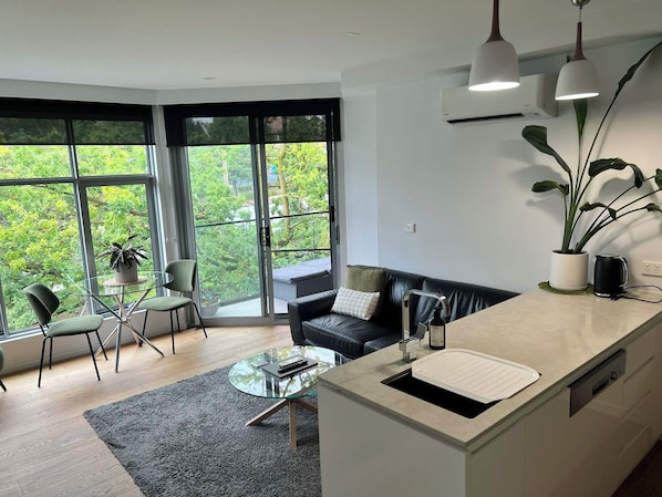 Et moderne køkken med et sofabord i glas, en sofa og et spiseområde med stole.