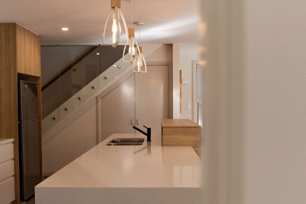 Une cuisine moderne dotée d’un îlot central, d’appareils électroménagers en acier inoxydable et d’un escalier en bois.